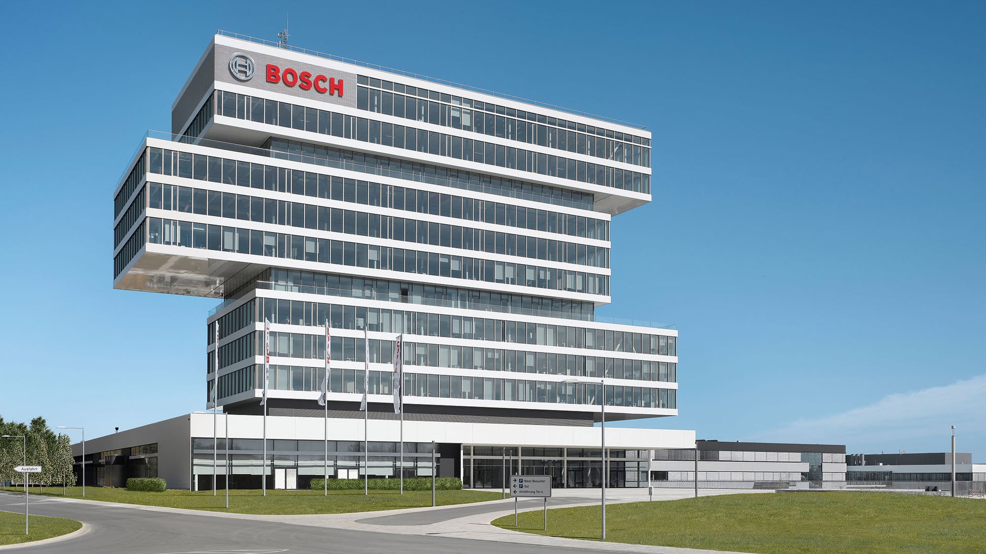 Bosch-Verwaltungsgebäude: ein weißer, auskragender Bau mit dem Bosch-Schriftzug auf dem Dach, umgeben von Wiesen