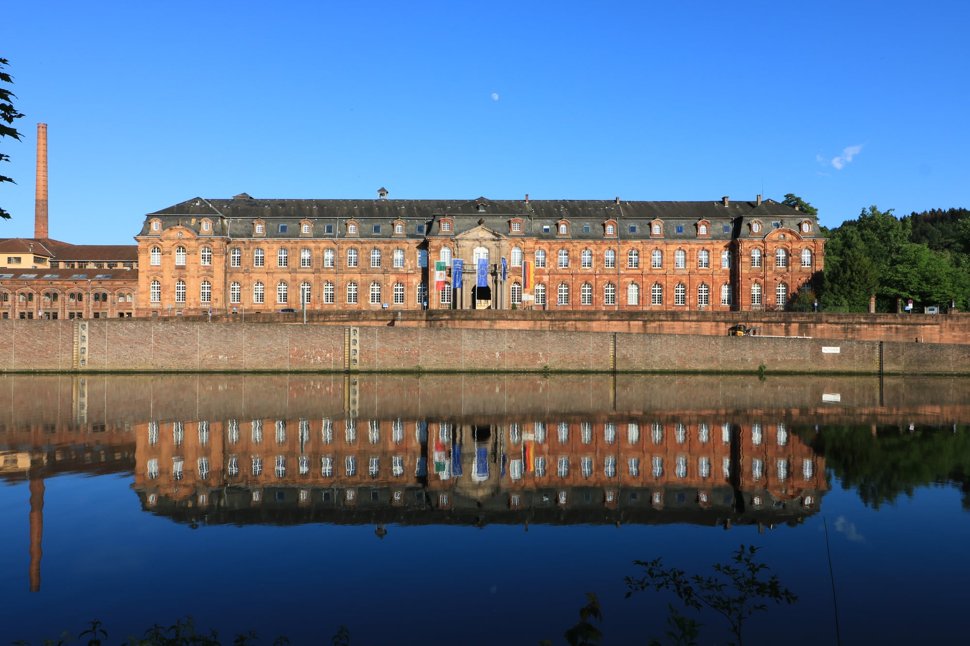 Historisches Werksgebäude von Villeroy & Boch aus rotem Backstein am Wasser, das sich in der spiegelglatten Oberfläche spiegelt