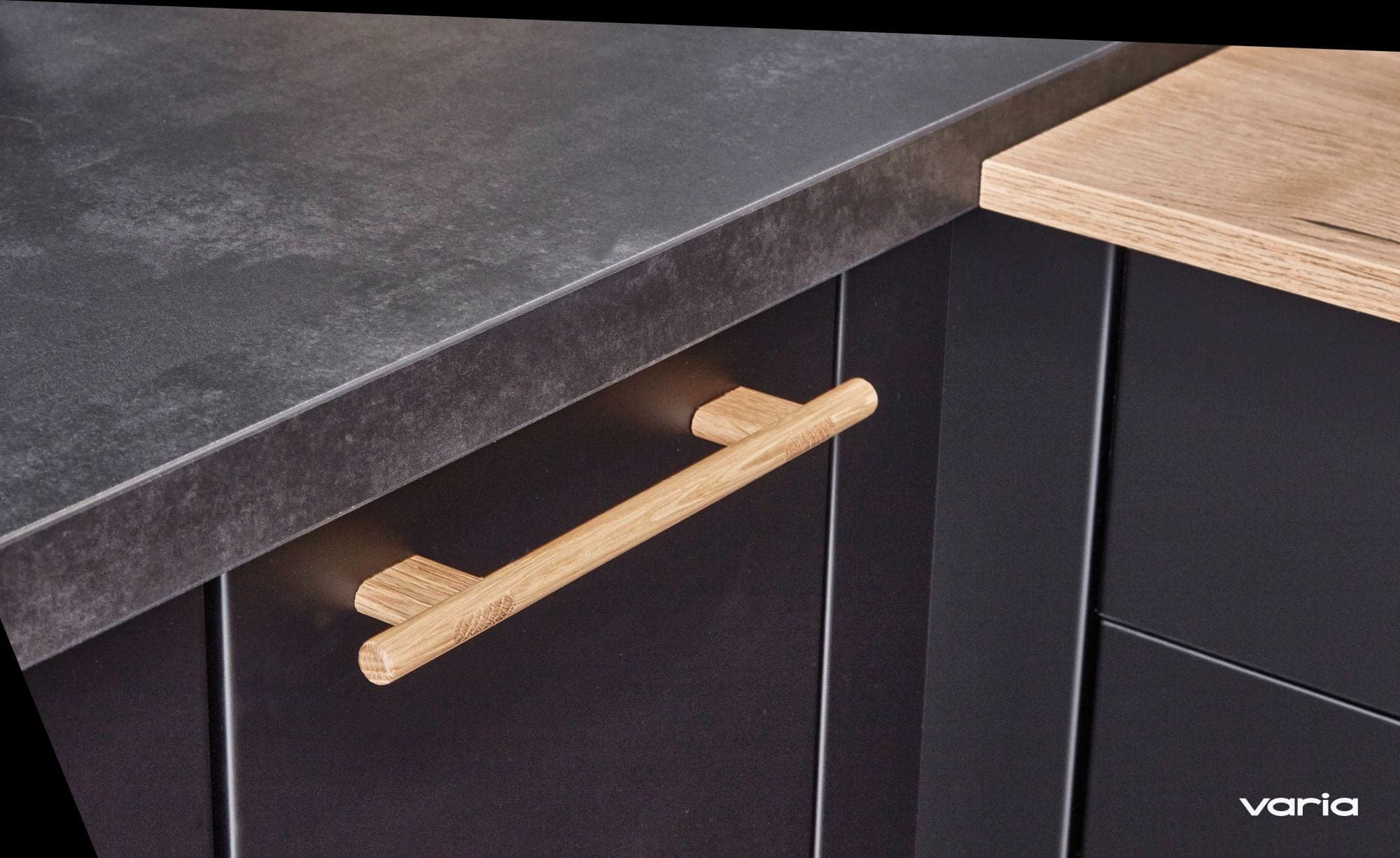 Arbeitsplatte in dunkler Steinoptik über einer schwarzen Front mit Holzgriff, die Kante im Detail