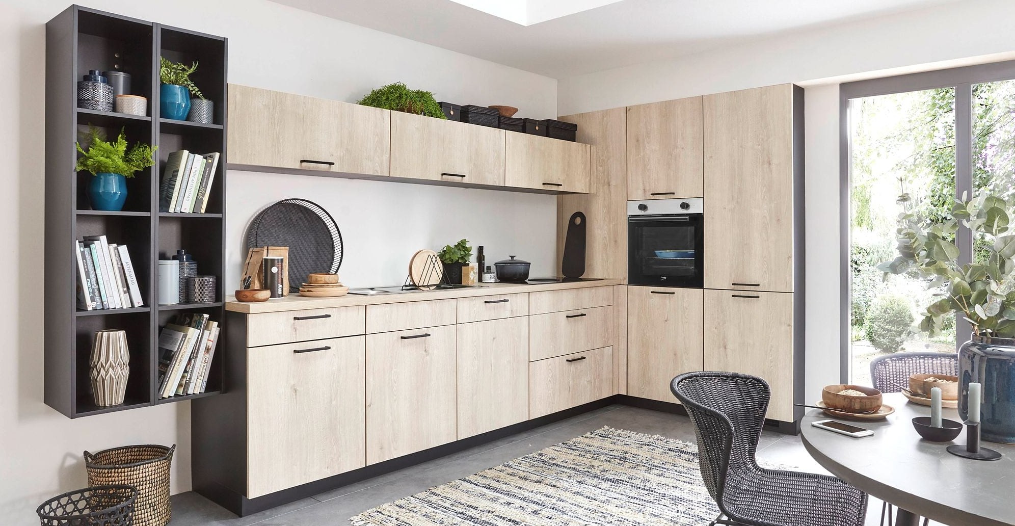 Helle Küche in Holzoptik, rechts eine offene Terrassentür mit Blick in einen begrünten Garten