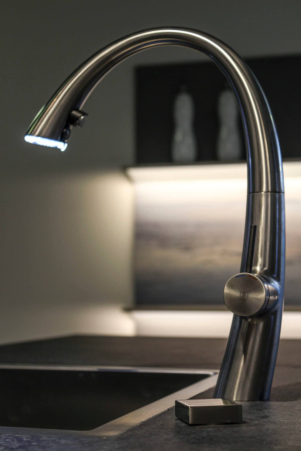 Edelstahl-Auszugsarmatur über einem dunklen Becken, im Spotlicht