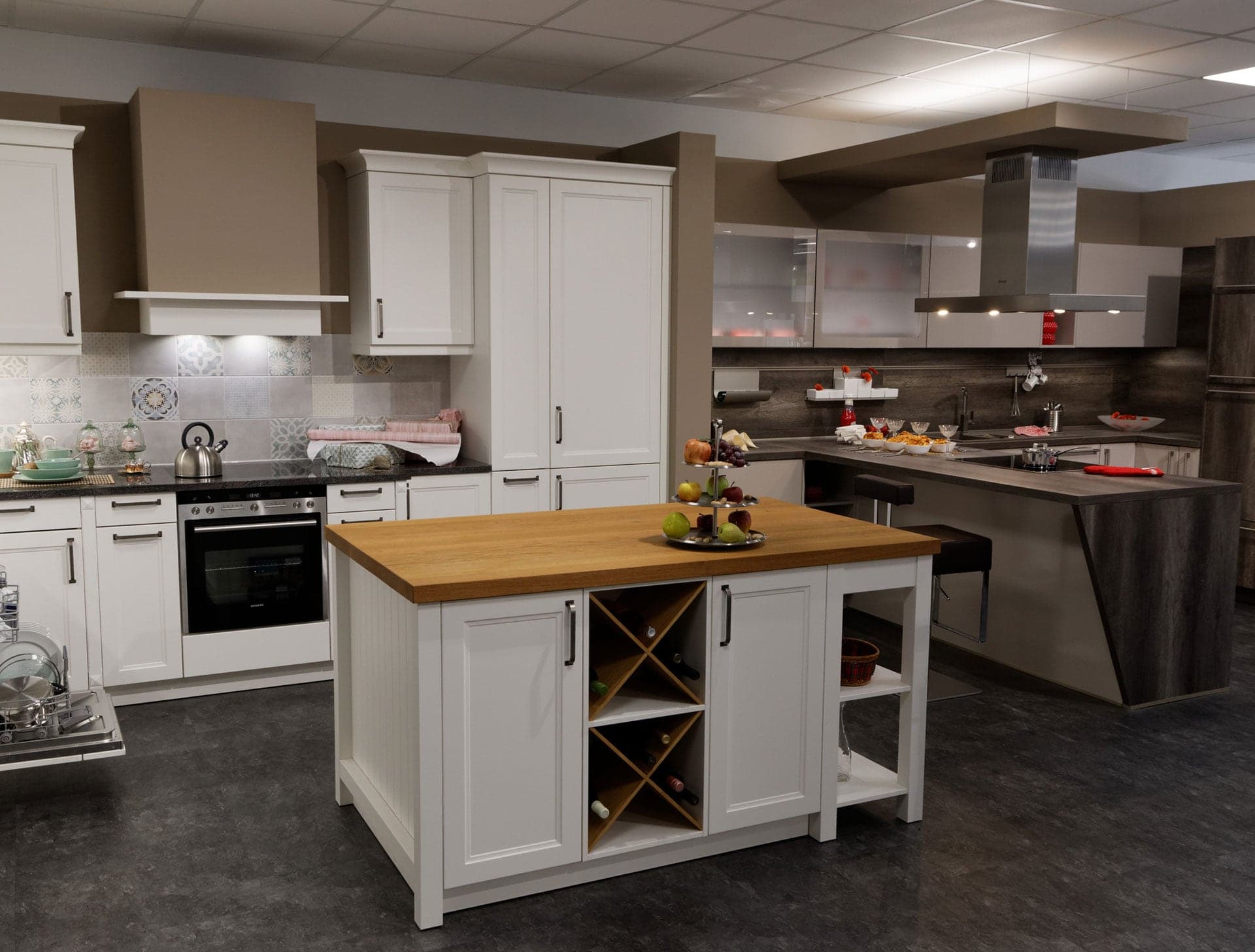 Weiße Landhausküche mit Holzinsel und offenem Weinregal, dahinter eine dunkle moderne Zeile