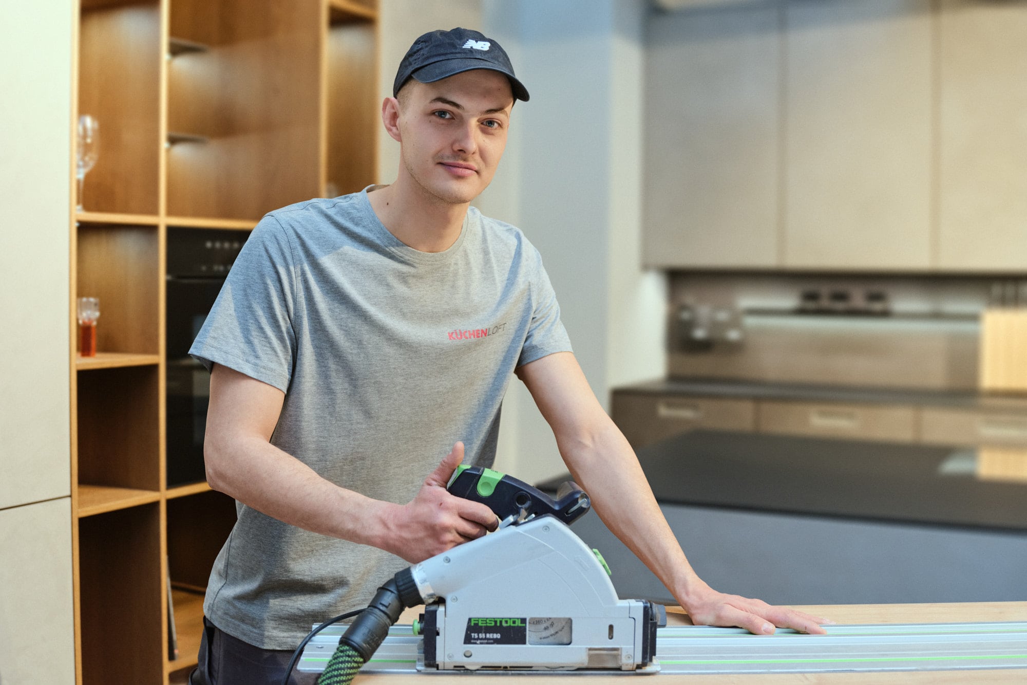 Montage im KüchenLoft Köln: ein Monteur im grauen KüchenLoft-Shirt steht mit der Tauchsäge an der Führungsschiene über einer Arbeitsplatte