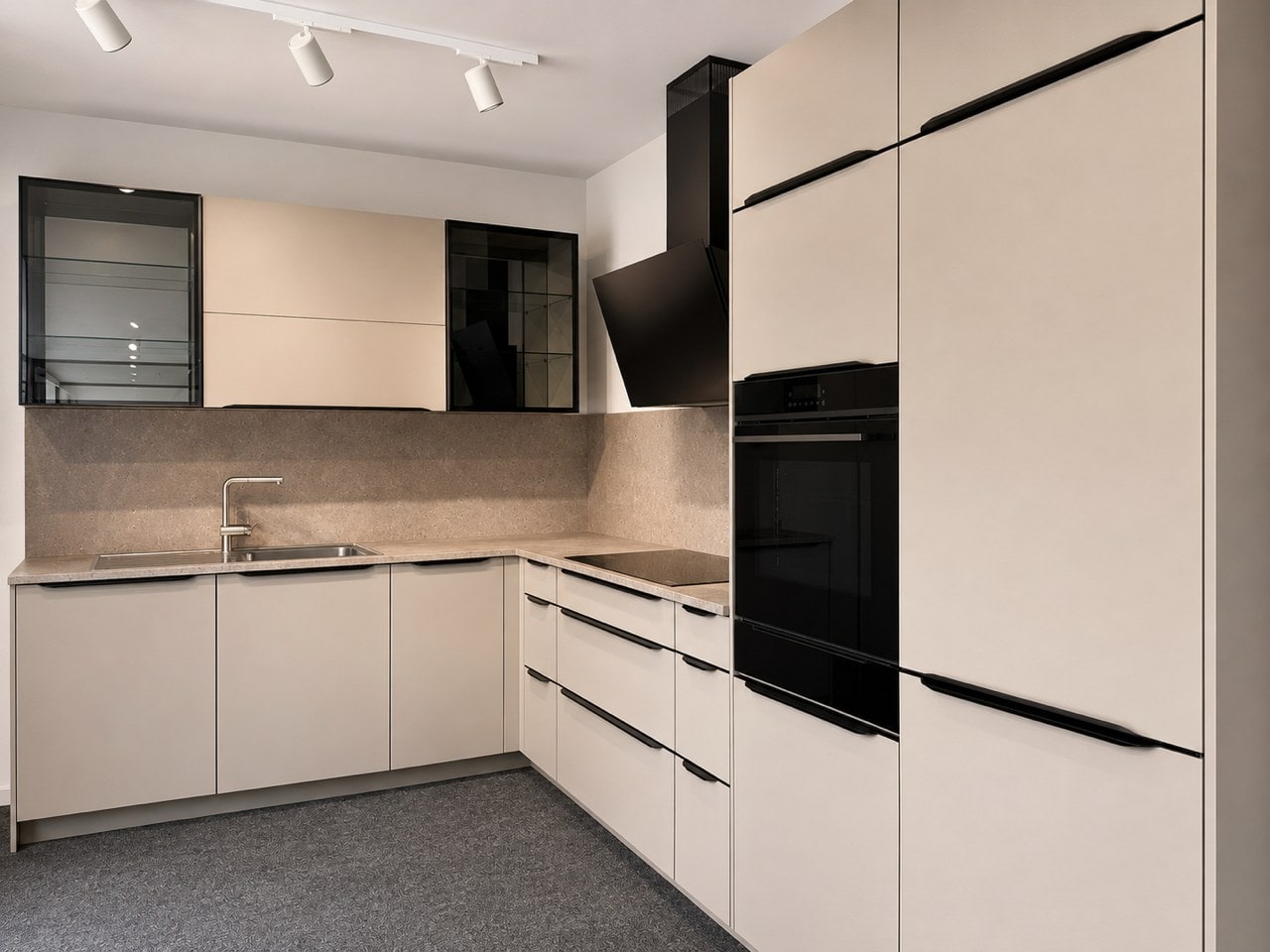 Helle Winkelküche in der Ausstellung in Ludwigsburg: matte sandfarbene Fronten mit schwarzen Griffleisten, Arbeitsplatte und Rückwand in Steinoptik, zwei Hängeschränke mit schwarz gerahmten Glastüren, eine schwarze Schräghaube und ein Hochschrank mit Backofen