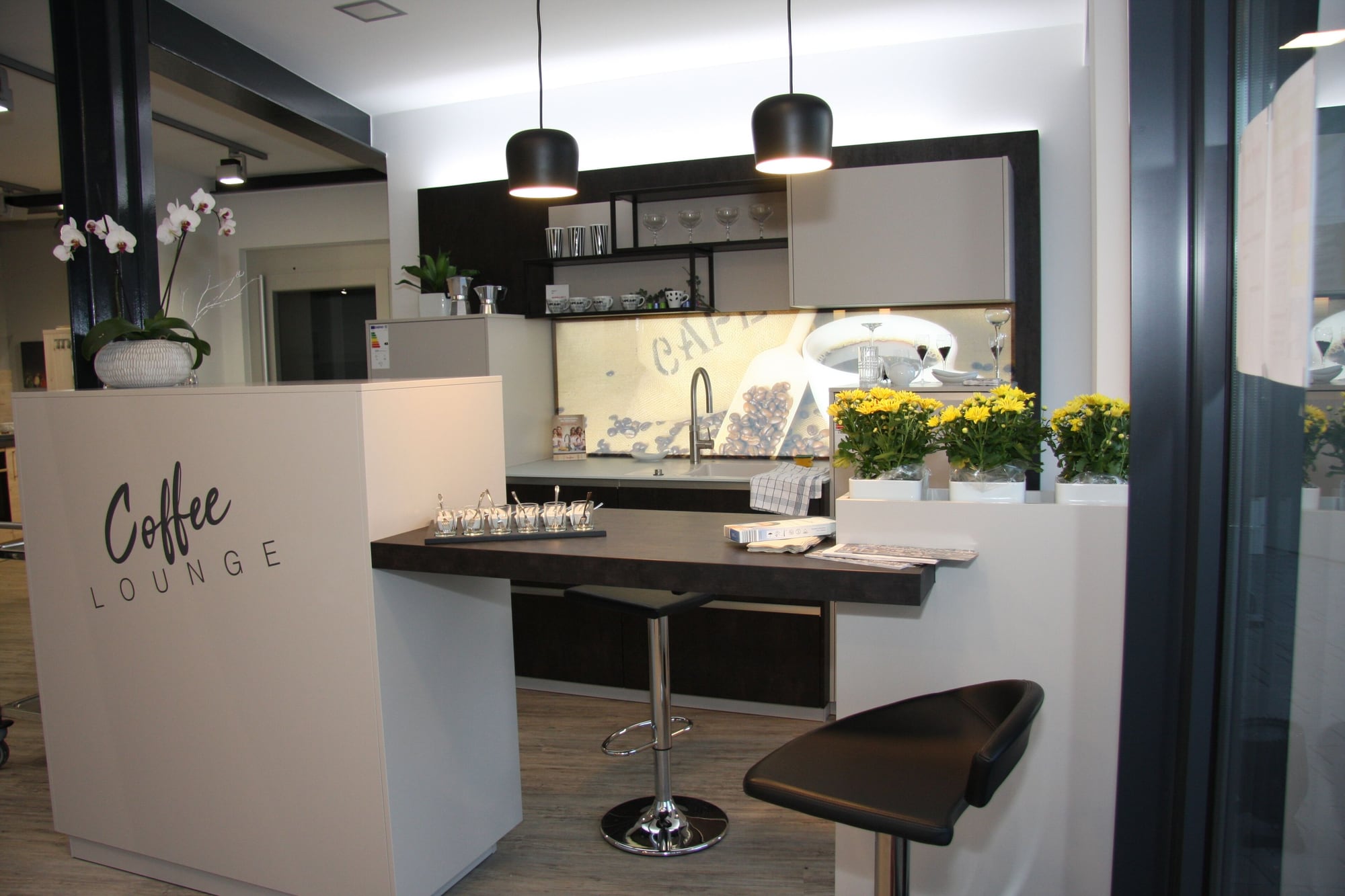 Coffee Lounge in der Ausstellung Welzheim: dunkler Bartisch mit Hocker, zwei schwarze Pendelleuchten, eine Rückwand mit Kaffeebohnen und der Schriftzug Coffee Lounge